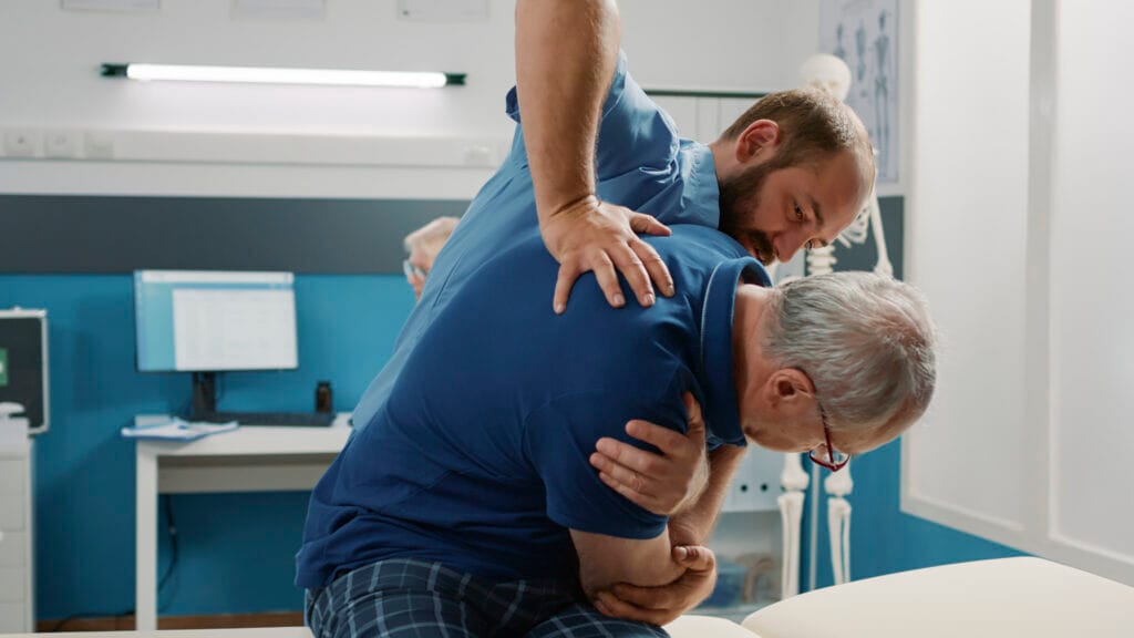 Osteopath helping senior man to crack back bones in cabinet