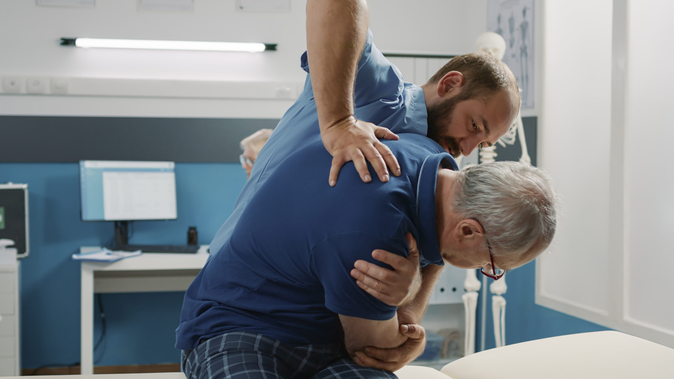Osteopath helping senior man to crack back bones in cabinet